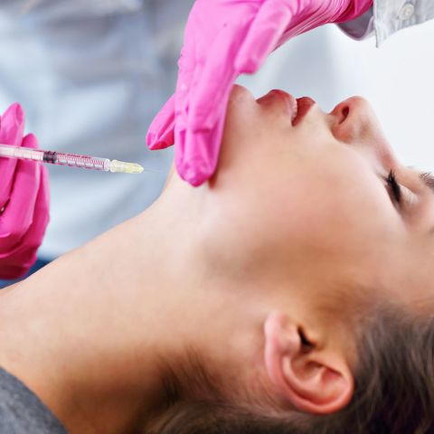 Behandlung einer jungen Frau: Spritze wird gerade in den Hals gesteckt